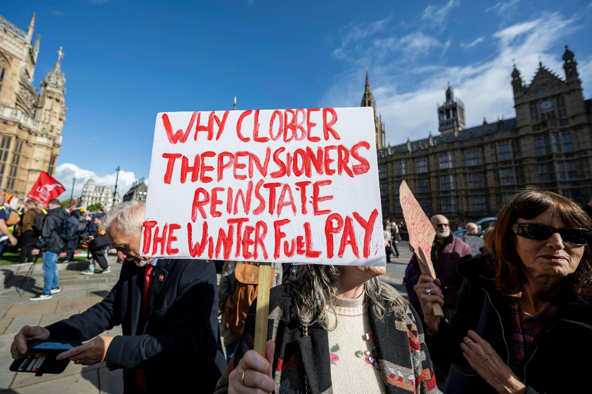 A protester holds a sign outside parliament against cuts to the winter fuel payment, reading 'why clobber the pensioners, reinstate the winter fuel pay'