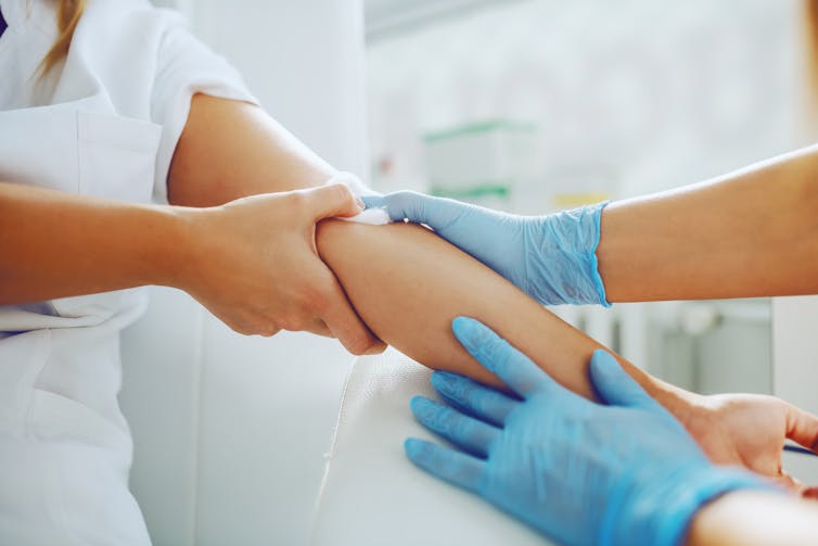 A medic pressing a cotton swab to a patient's arm.