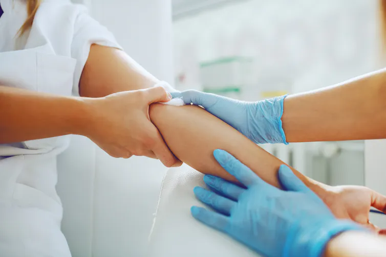 A medic pressing a cotton swab to a patient's arm.