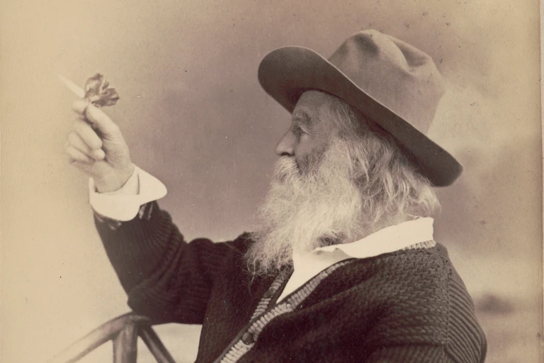 Sepita toned photograph of bearded man wearing a hat and sweater, balancing a butterfly on his fingertip.