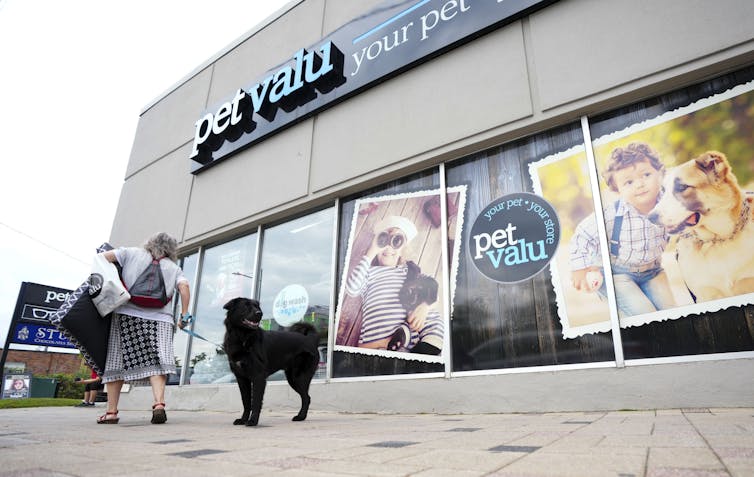 Una mujer y un perro negro frente a la tienda de mascotas