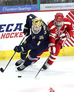 Two hockey players race for the puck along the boards.
