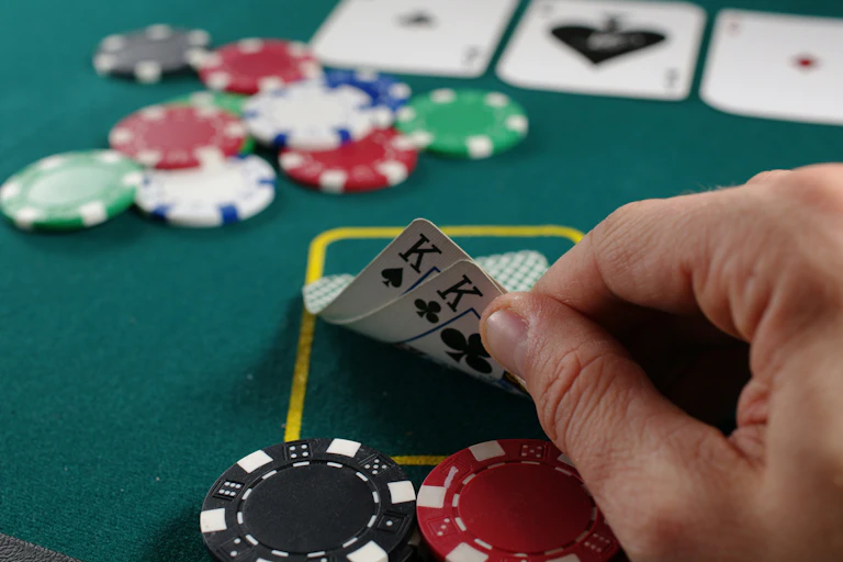 a green table with plastic chips and playing cards, A hand holds cards, revealing 2 kings.
