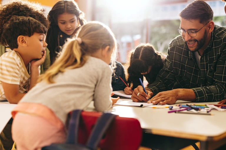 Un maestro rodeado de niños y niñas en el aula