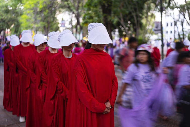 People in red cloaks in a sombre line.