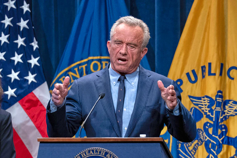 A man at a podium with yellow flag behind him.