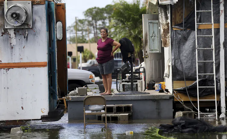 A woman stands on a porch of a home damaged by the storm and surrounded by flooding.