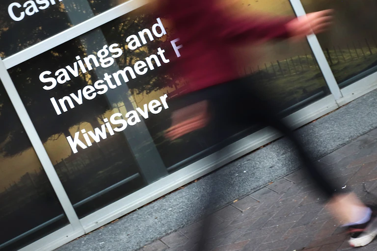 Woman walks past glass storefront advertising KiwSaver