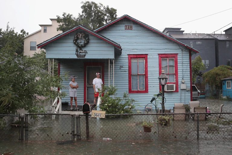 People stand on a porch as water fills their yard.