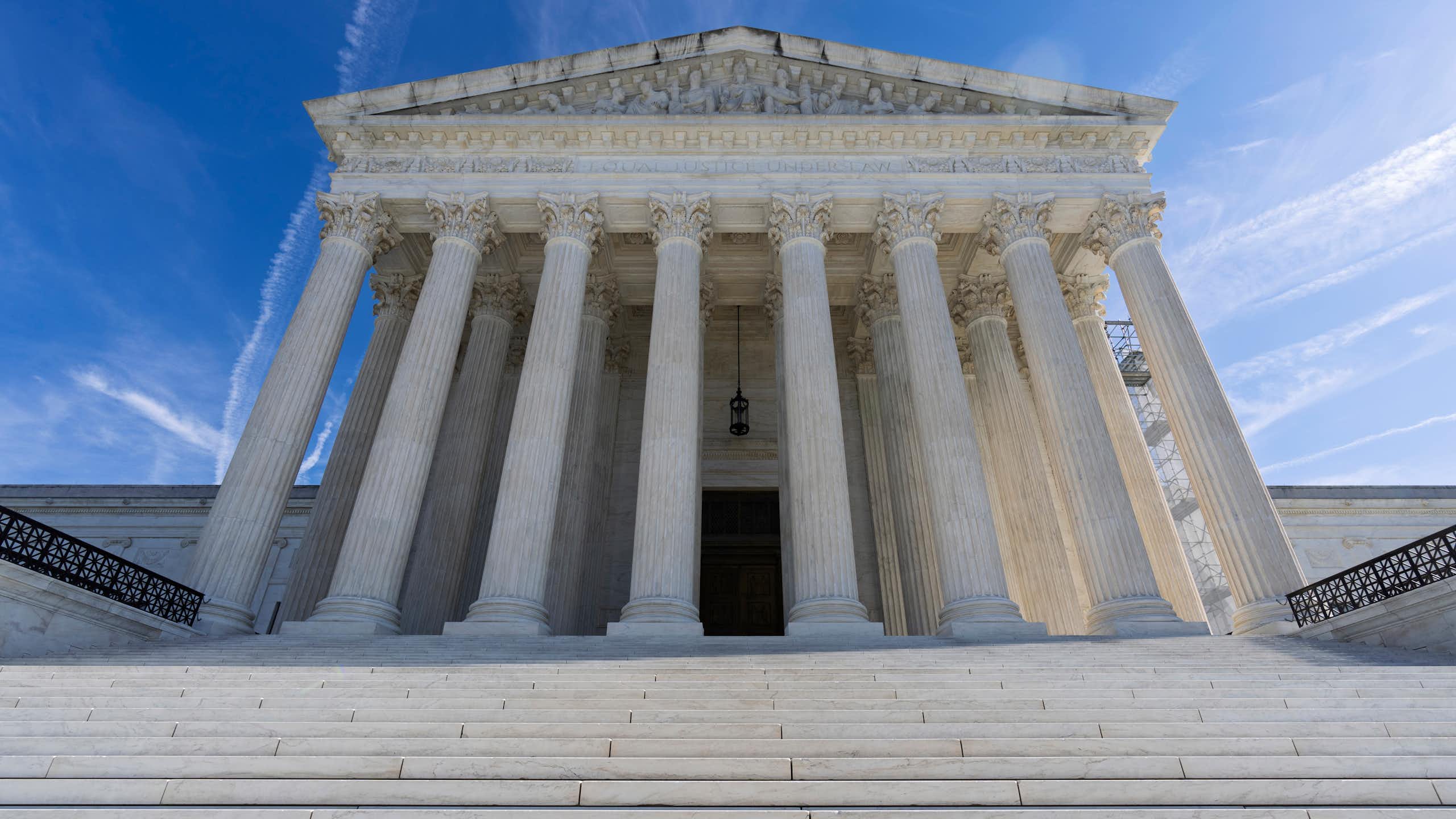 A large white building with pillars, viewed from the bottom of steps leading up to it.