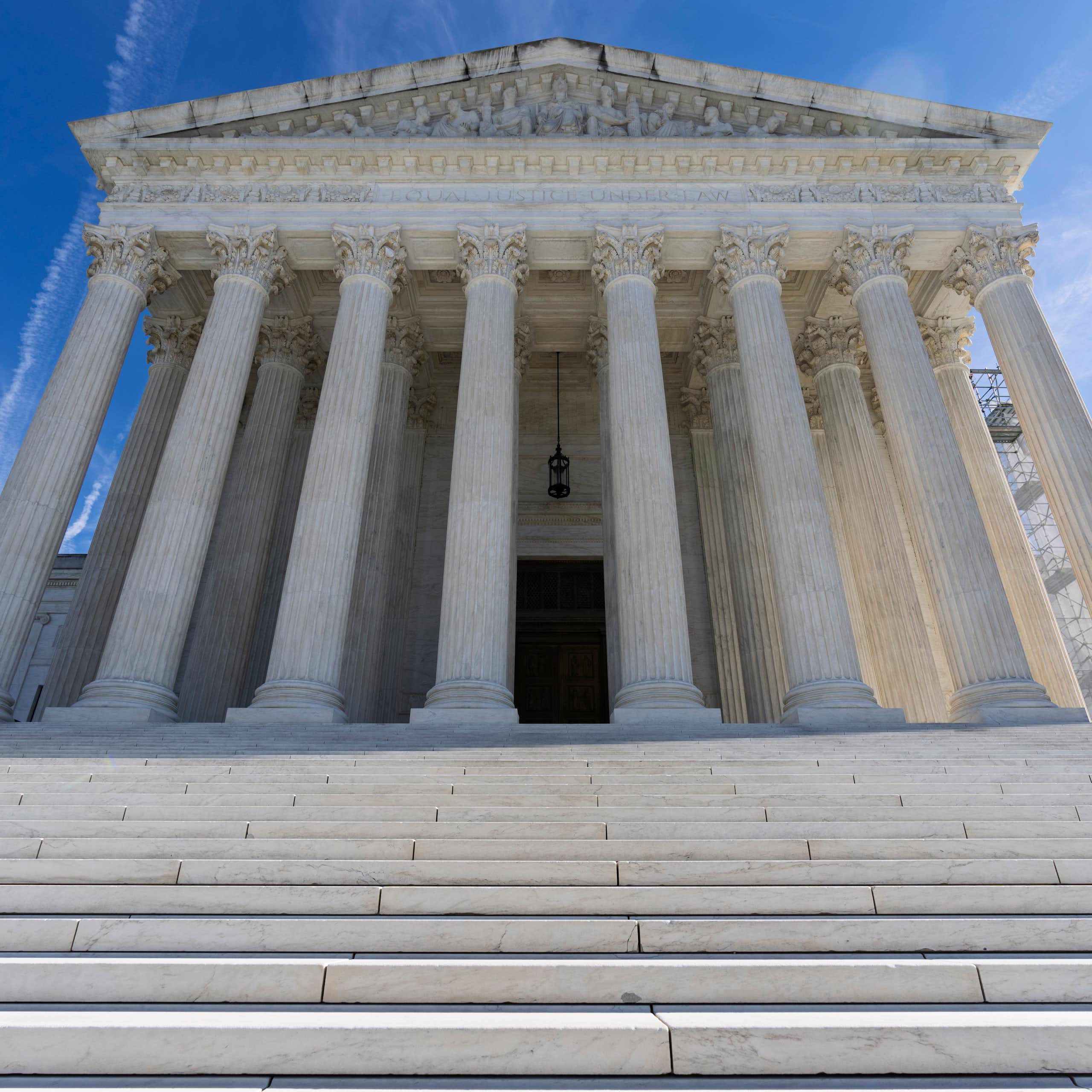 A large white building with pillars, viewed from the bottom of steps leading up to it.