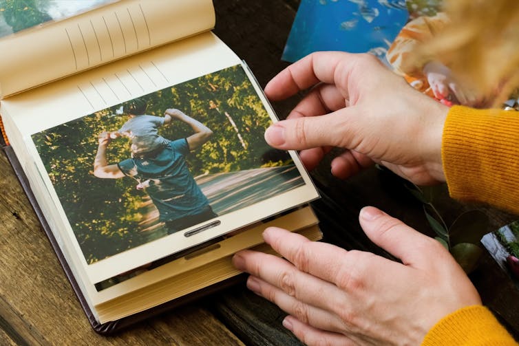 Hands touching an open album with a photo of a kid on dad's shoulders.
