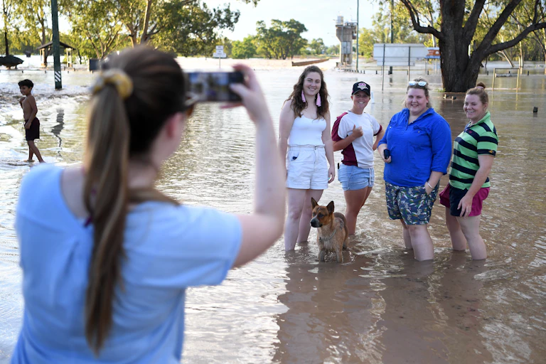 A woman takes a photo of four people and a dog in floodwaters