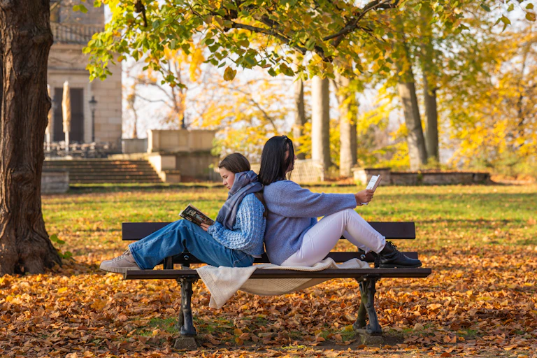 Dos personas leyendo en un parque, espalda con espalda