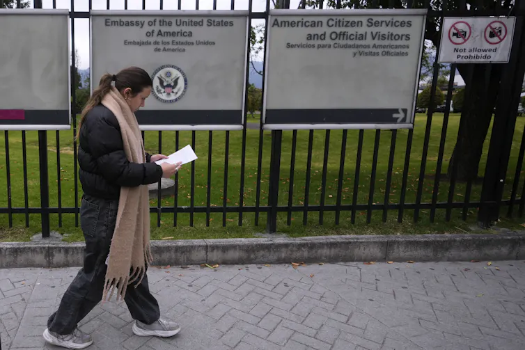 A woman with her head bowed before a sign that says U.S. Embassy.