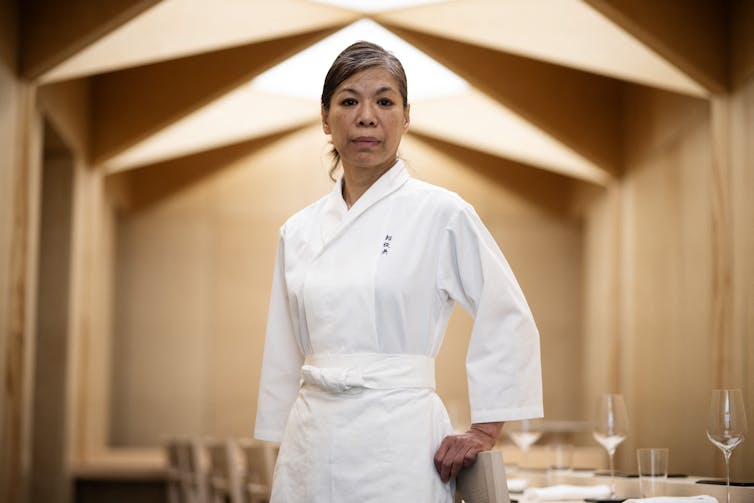 Woman in crisp white chef uniform stands in sleek restaurant