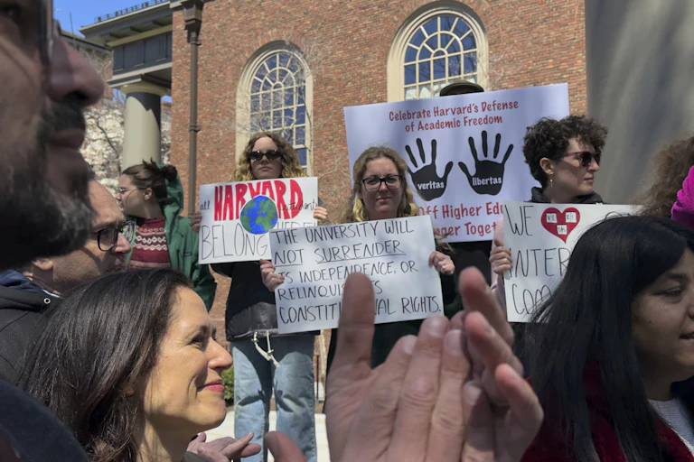 People stand at a rally with signs, one says the university will not surrender its independence.