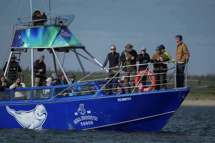 People stand on the deck of a small blue boat that says 'Sea North Tours' on the side