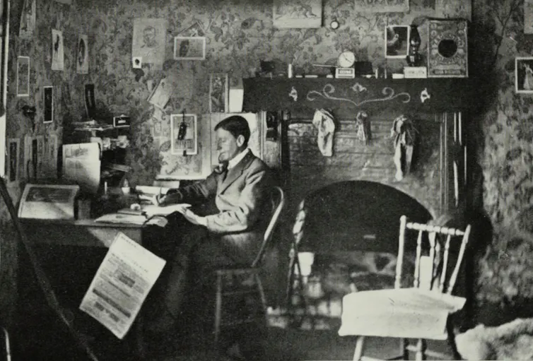 A man (C.J. Dennis) at his desk writing.