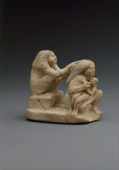 A woman is shown nursing her child while another woman is dressing her hair.