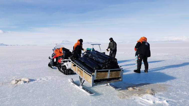 Three people with a sled travelling on sea ice in McMurdo Sound.