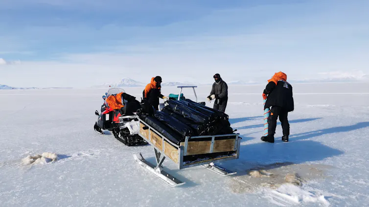 Three people with a sled travelling on sea ice in McMurdo Sound.