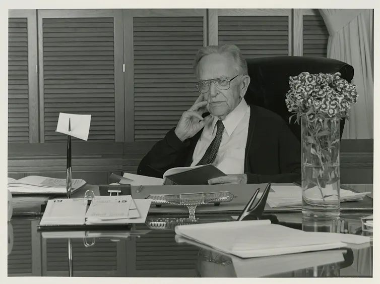 A black and white historical image of an elderly man sitting at his desk