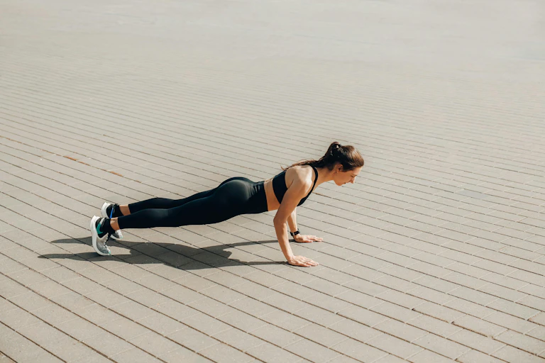 A woman doing a plank outdoors on concrete pavement.