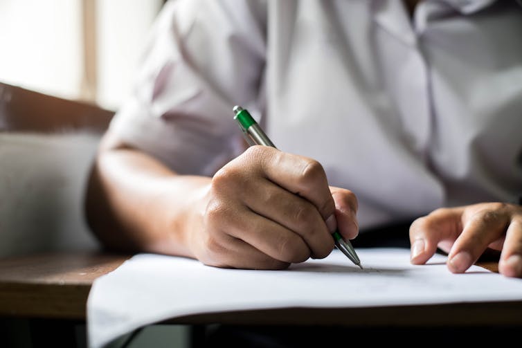 An older student writes with a pen on a paper.