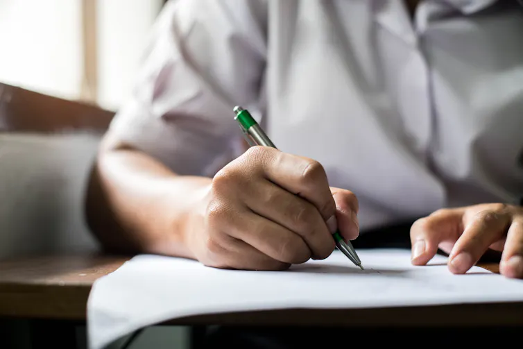 An older student writes with a pen on a paper.