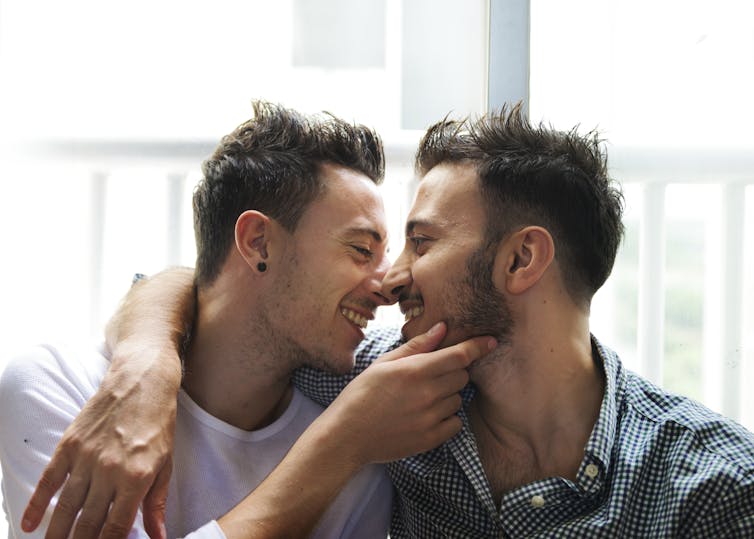 Two men gently embrace and smile while looking into one another's eyes.