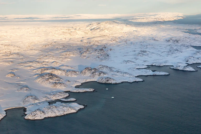 Vue aérienne d'un paysage côtier recouvert de neige ou de glace sous un ciel alternativement clair et nuageux.