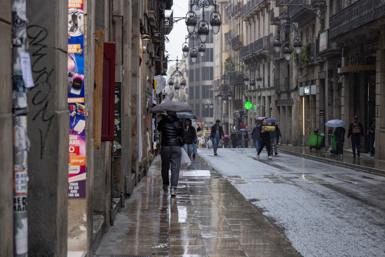 Calle de Barcelona con el suelo mojado y gente con paraguas