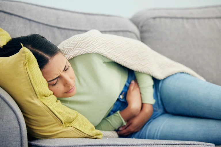 Mujer recostada en sofá con dolor abdominal
