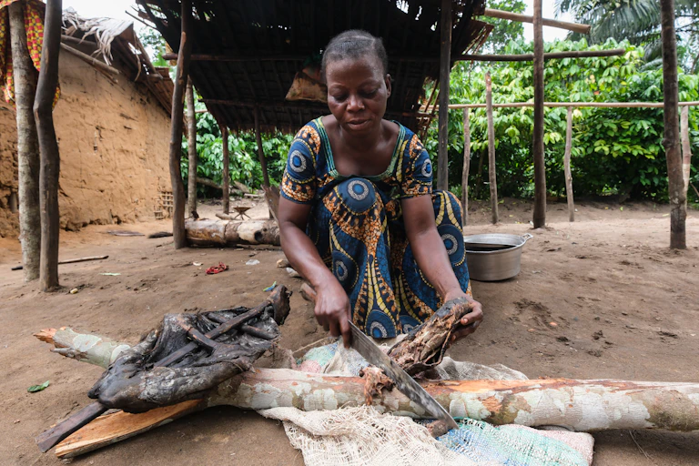 A woman chopping up a medium-sized piece of meat that she has placed on a piece of wood