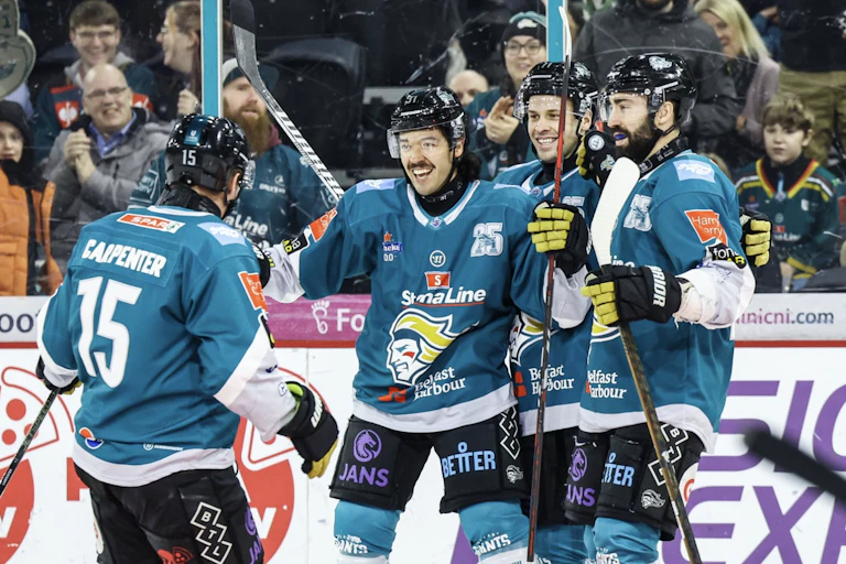 Hockey plays in turquoise and white uniforms smile as they celebrate a goal.
