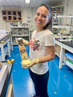 a woman holding a tube filled with layers of different coloured sediment