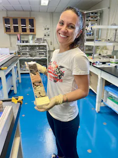 a woman holding a tube filled with layers of different coloured sediment