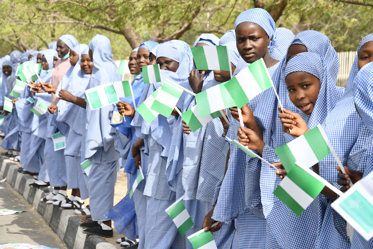 Girls wearing identical robes and headscarves, holding green and white flags