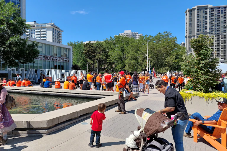 A group of people gathered in front of a fountain and a large sign reading Hamilton