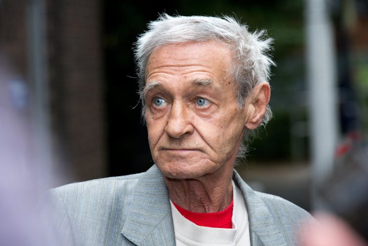Photo of a man with grey hair in a grey suit.
