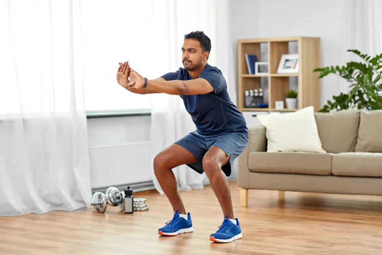 A man performs a bodyweight squat in his home.