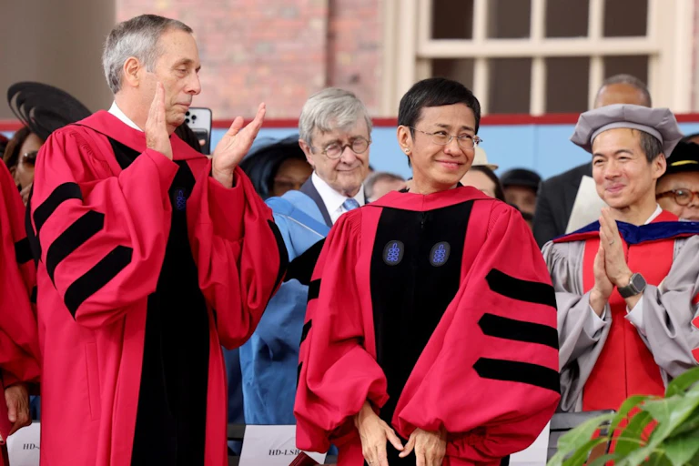 People gather at a Harvard graduation ceremony in 2024, wearing red robes.