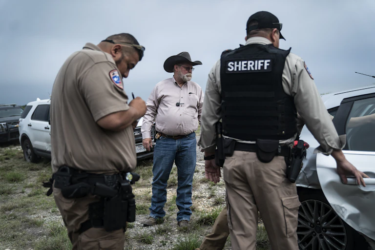 Two sheriffs watch as another sheriff places a man into a patrol car.