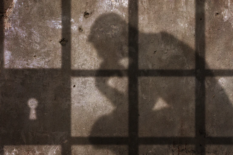 Shadow on a concrete wall of a thinking man statue behind locked bars