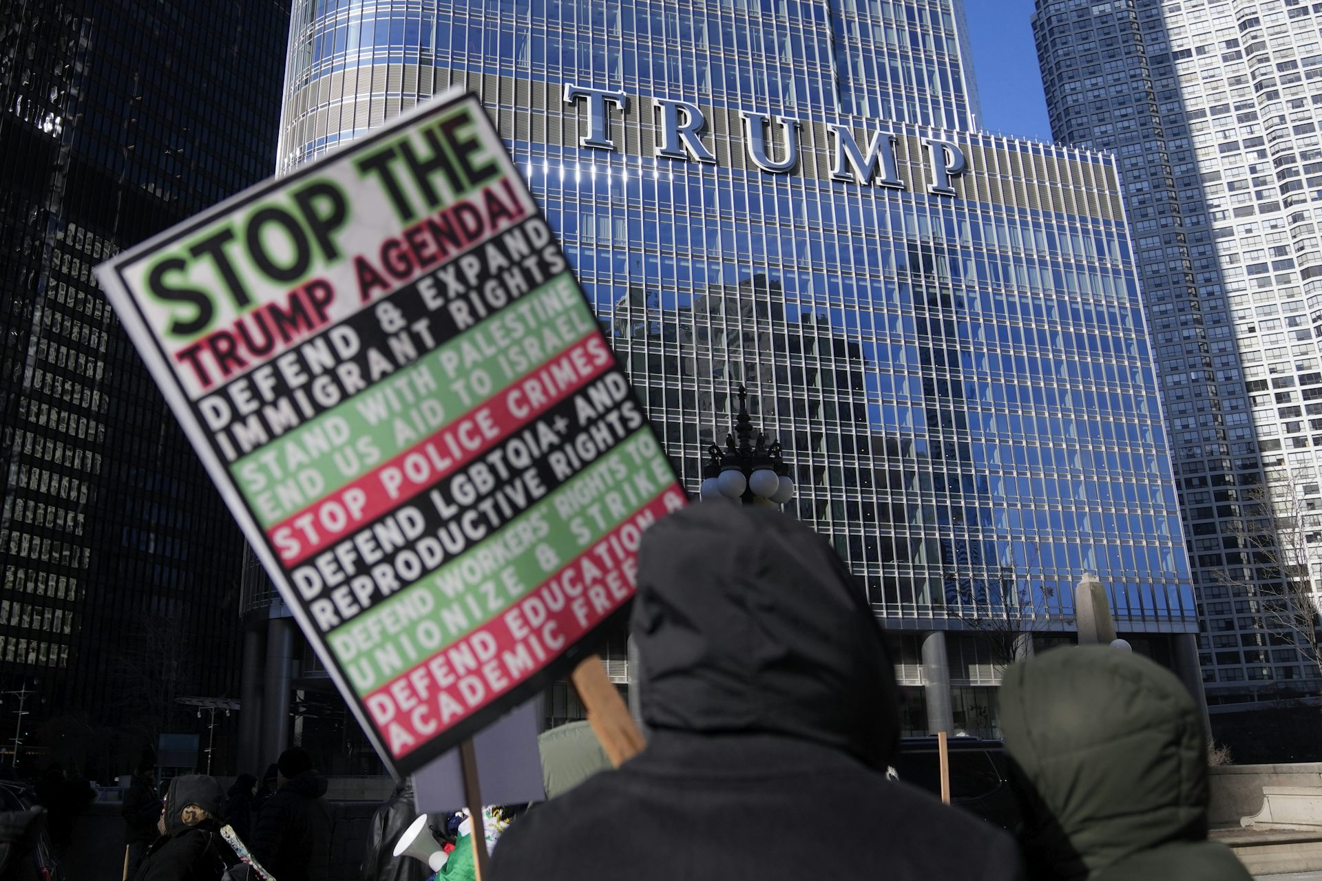 A proteser carries a sign listing grievances against Donald Trump with the Trump Tower in the background.