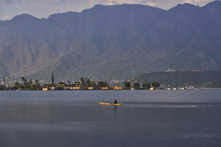 A lake with a yellow boat on it and mountains in the background.