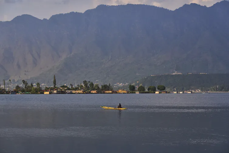 A lake with a yellow boat on it and mountains in the background.