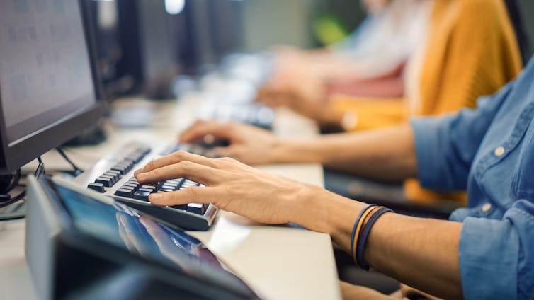Close up of a pair of hands typing on a keyboard in front of a computer monitor at a cubicle