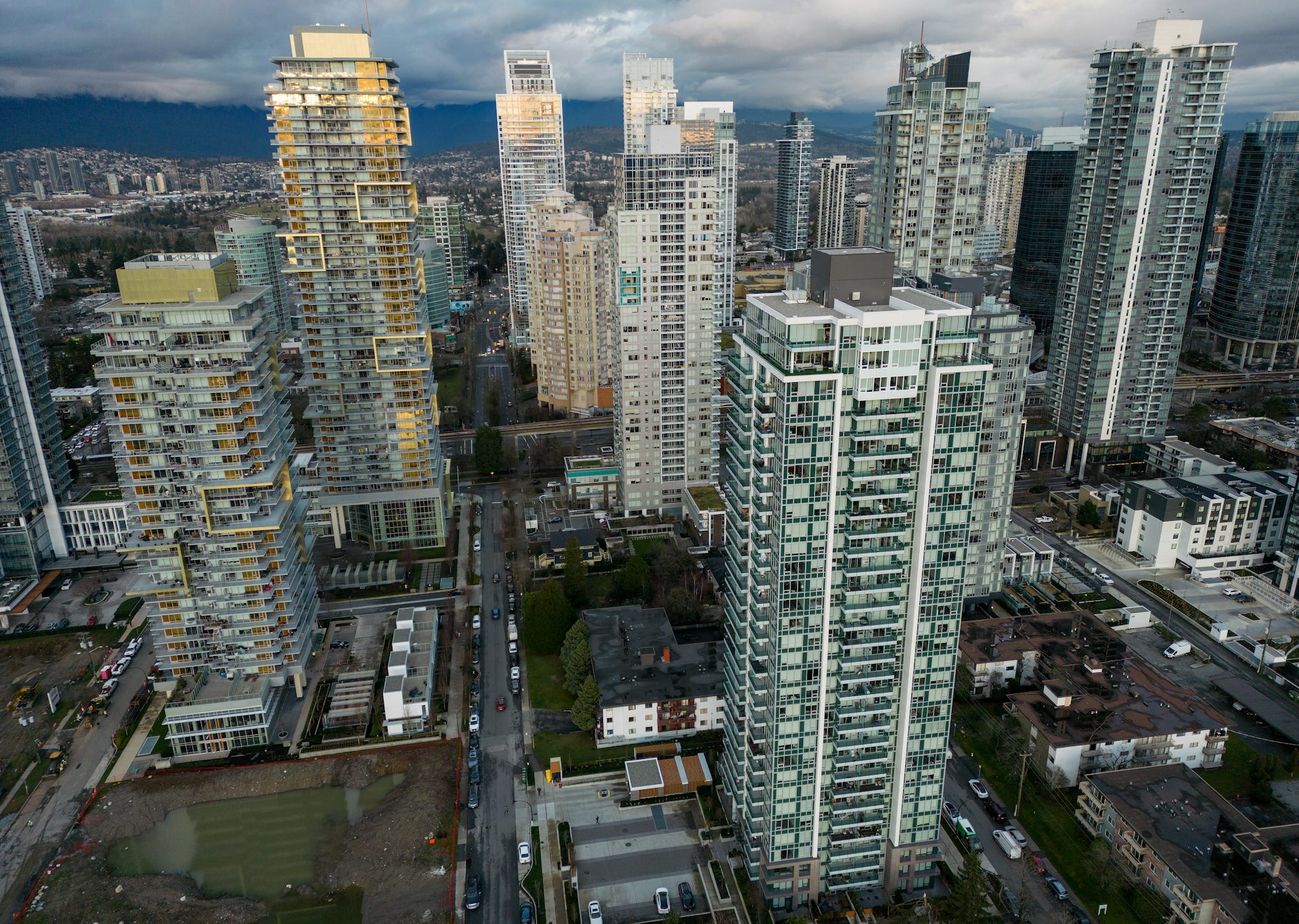 An aerial view of condo buildings with a grey sky and mountains in the background.